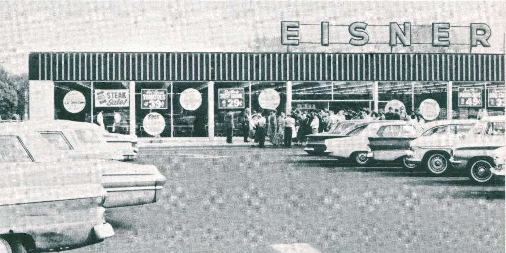 People outside Eisner store, vintage cars parked.